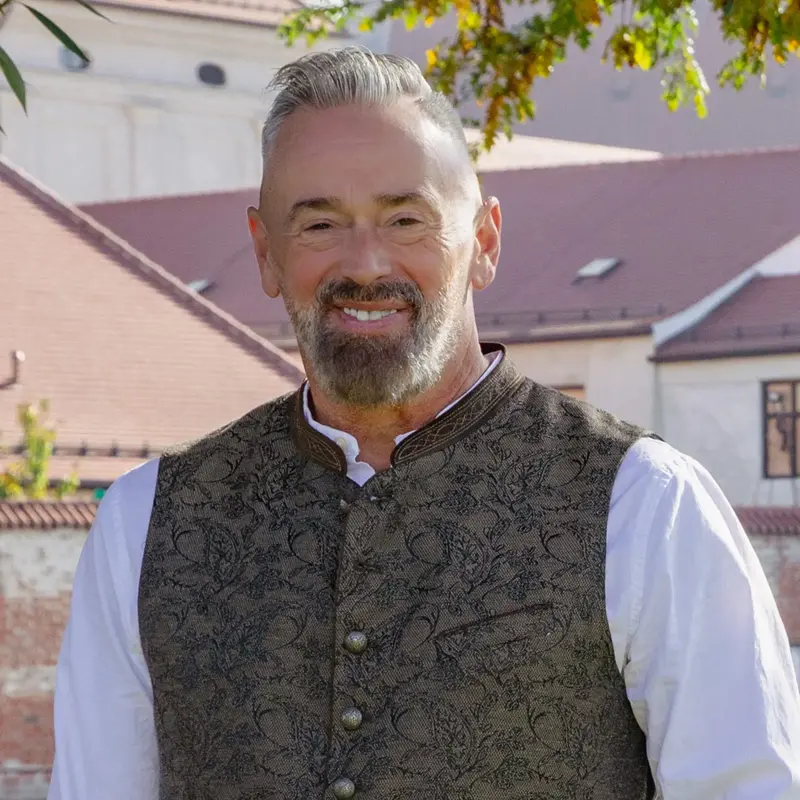 Ein Mann in traditioneller Kleidung lächelt vor historischer Kulisse, passend zur Kommunalwahl 2026 in Landshut.