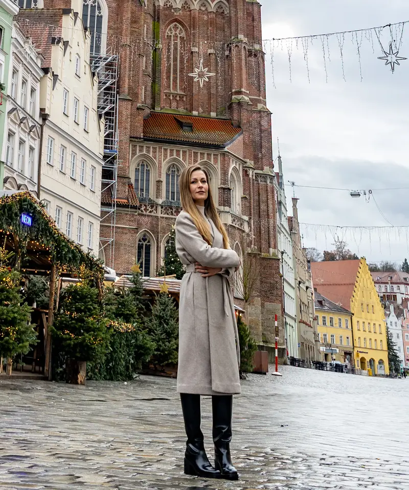 Eine Frau steht selbstbewusst vor der Kirche in Landshut, möglicherweise als Stadtratskandidatin für die Kommunalwahl 2026.
