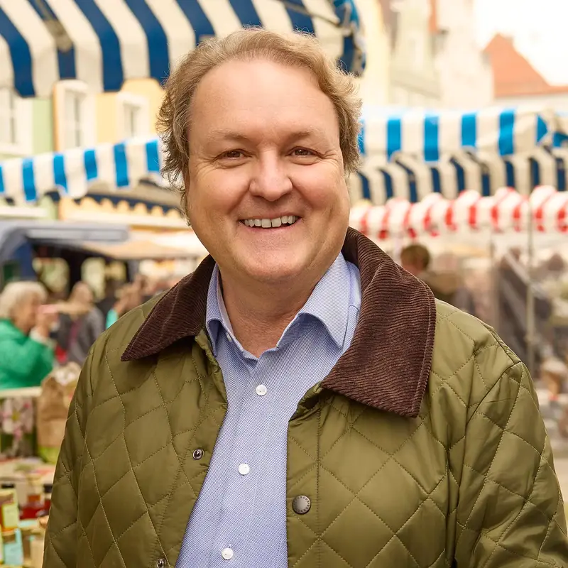 Ein lächelnder Mann steht auf einem Markt in Landshut, möglicherweise ein Stadtratskandidat für die Kommunalwahl 2026.