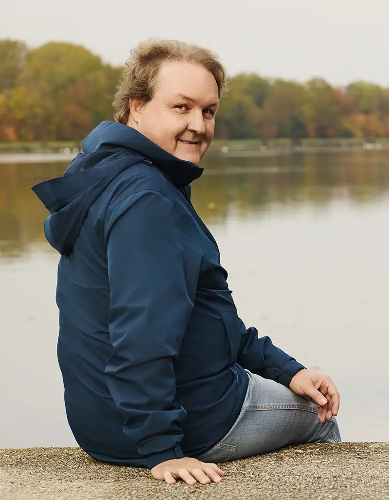 Ein Mann sitzt lächelnd am Seeufer in Landshut, möglicherweise als Stadtratskandidat für die Kommunalwahl 2026.